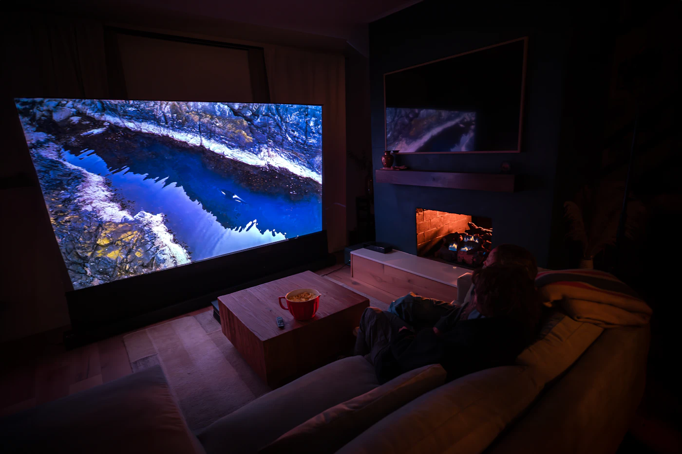 A person relaxing on a sofa in front of a large wall-mounted screen showing a nature scene
